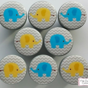 Peut inclure: Huit boutons ronds avec un motif chevron gris et un motif d'éléphant. Quatre boutons présentent un éléphant bleu et quatre boutons présentent un éléphant jaune.