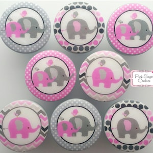 May include: A collection of eight decorative cabinet knobs. Each knob features a pink and gray elephant design with a small bird on top. The knobs have various patterned borders in gray and pink, including polka dots and chevron.