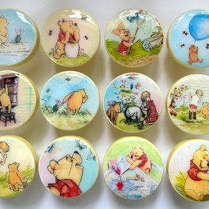 Könnte beinhalten: Eine Sammlung von zwölf runden Schrankknöpfen mit Illustrationen von Winnie Puuh und seinen Freunden. Jeder Knopf hat einen cremefarbenen Rand und zeigt eine andere Szene, darunter Puuh mit Honig, Ferkel und einen blauen Ballon.