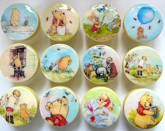 May include: A collection of twelve round cabinet knobs featuring illustrations of Winnie the Pooh and friends. Each knob has a cream-colored border and a different scene, including Pooh with honey, Piglet, and a blue balloon.