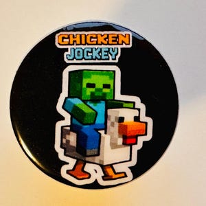 May include: A black and white button featuring a green zombie riding a white chicken. The button displays the text "CHICKEN JOCKEY" in orange and blue.