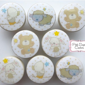 May include: Set of eight round wooden knobs with a white background and a light brown polka dot pattern. Each knob features a different animal illustration: a duck, a sheep, a bear, a rabbit, a duck, a sheep, a rabbit, and a bear. The knobs are perfect for adding a touch of whimsy to any nursery or child's room.