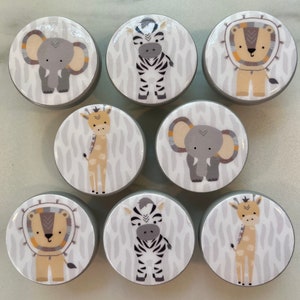 Può includere: Set di 8 pomelli rotondi in legno grigio con illustrazioni di animali. Gli animali includono una zebra, una giraffa, un leone e un elefante. Ogni pomello ha uno sfondo bianco con illustrazioni di animali grigi.