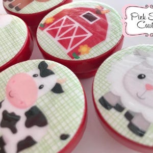 May include: Set of six red round favor boxes with farm animal designs. Each box features a different animal, including a cow, a sheep, a chicken, and a barn. The boxes are decorated with a green and white checkered pattern.