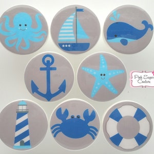 May include: Set of eight blue and white nautical themed stickers with a gray background. The stickers feature an octopus, sailboat, whale, anchor, starfish, lighthouse, crab, and life preserver.