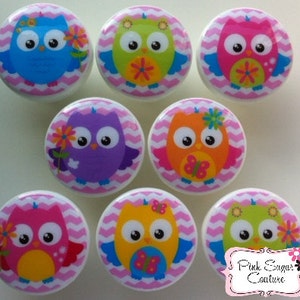 Może przedstawiać: Osiem okrągłych gałek do szafek z kolorowymi wzorami sów. Każda gałka ma białą podstawę z różowo-białym wzorem w zygzaki. Sowy są w różnych kolorach, w tym niebieskim, zielonym, różowym, fioletowym, pomarańczowym i żółtym. Ozdobne.