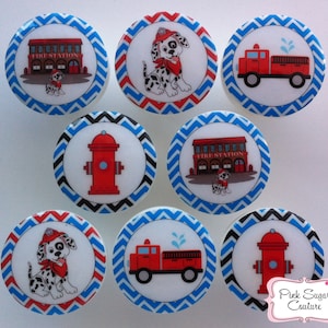 Pode incluir: Conjunto de oito toppers redondos de papel branco de 5 cm de diâmetro com um padrão de chevron azul e vermelho. Os toppers apresentam imagens de uma estação de bombeiros, um caminhão de bombeiros, um filhote dálmata e uma boca de incêndio.