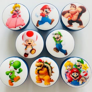 May include: Eight round cabinet knobs with cartoon character designs. Each knob has a white face with a blue edge. Characters include Princess Peach, Mario, Donkey Kong, Toad, Luigi, Yoshi, Bowser, and a group shot of Mario, Peach, Luigi, Toad, and a star.