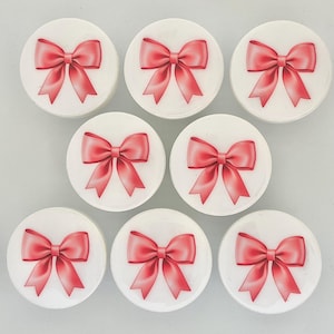 May include: Seven round white stickers with a pink bow printed on each. The bows are all facing the same direction.