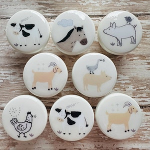 May include: Set of eight white ceramic knobs with farm animal illustrations. The knobs feature a cow, horse, pig, goose, goat, and chicken. The knobs are approximately 5 cm in diameter.