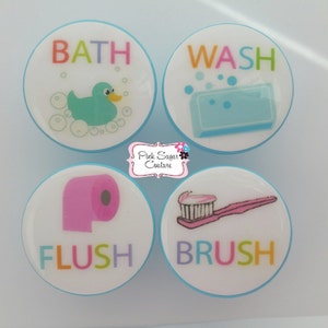 May include: Four round, white, blue-rimmed bathroom themed knobs with colorful text and images. The knobs read "BATH" with a rubber duck, "WASH" with a bar of soap, "FLUSH" with a toilet paper roll, and "BRUSH" with a toothbrush.