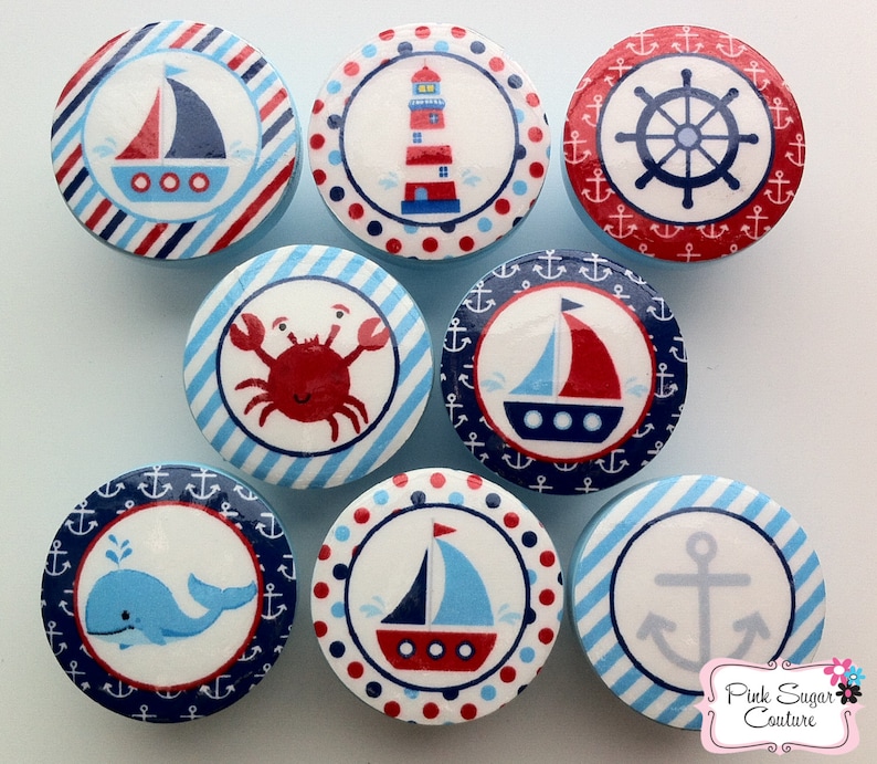 May include: Nine round, blue and white nautical themed knobs with various designs including a lighthouse, sailboat, anchor, crab, whale, and a ship's wheel.  The knobs are decorated with red, blue, and white stripes, polka dots, and anchors.
