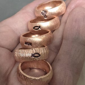 May include: Five gold-colored rings with different engravings. The top ring has a cross, the next ring has a fish symbol, the third ring has the word "HOPE", the fourth ring has a fish symbol, and the bottom ring is plain.