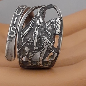 May include: A silver ring with a detailed design of a person riding a horse. The ring is inscribed with the word "LOUIS".