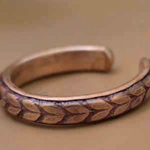 May include: A copper-colored ear cuff with a leaf pattern. The open-ended cuff curves around, showcasing the detailed design. The metal has a slightly aged appearance, adding to its vintage charm.