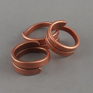 May include: Three copper rings with a simple, minimalist design. The rings are stacked on top of each other, and the top ring is slightly offset from the other two.