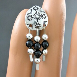 May include: Silver dangle earrings with a geometric design and black beads.
