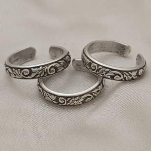 May include: Three silver toe rings with a floral design. The rings are adjustable and can be worn on any toe.