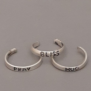 May include: Three silver toe rings with the words "BLISS", "PRAY", and "HUG" engraved on them.