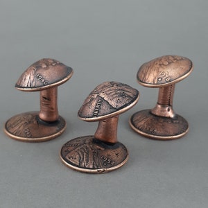 May include: Three copper cufflinks shaped like mushrooms, each with a different year inscribed on the top: 1946, 1952, and 1978.