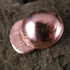 May include: A copper penny has been transformed into a small, dome-shaped hat. The Lincoln Memorial is visible on the side of the penny.