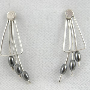 May include: A pair of silver earrings with a triangular design and dangling black beads.