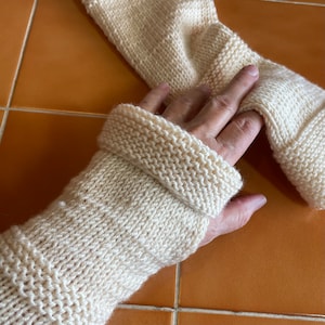 May include: A pair of cream knitted wrist warmers with a folded cuff. The warmers are made from a soft, textured yarn.