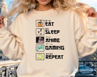 May include: A cream-colored sweatshirt with a graphic print of a list of activities in Japanese and English. The list includes "Eat", "Sleep", "Anime", "Gaming", and "Repeat".