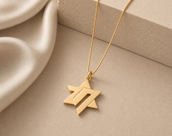 May include: A gold-toned necklace featuring a six-pointed Star of David pendant with a stylized, geometric cutout design. The pendant hangs from a delicate, thin gold-toned box chain, creating a simple and refined piece of jewelry.