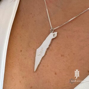 May include: A silver necklace with a pendant shaped like the outline of Israel. The pendant has a small diamond in the centre and the word "Israel" inscribed on it.