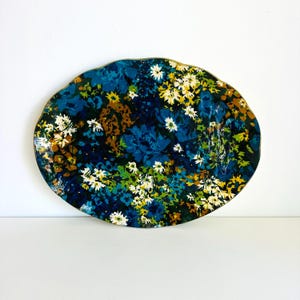 May include: An oval-shaped serving platter featuring a dense, multi-coloured floral pattern. The design includes shades of deep navy blue, bright teal, forest green, mustard yellow, and white flowers against a dark, saturated background.