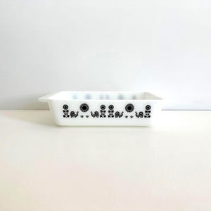 May include: White rectangular Pyrex baking dish with a black rooster, sunflower, and floral pattern. The dish has a simple, classic design with a slightly flared rim. A vintage kitchenware item.