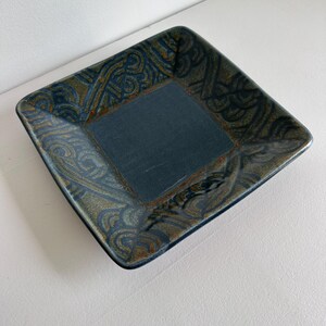 May include: Square ceramic dish with a blue glaze and a brown and gold patterned border.