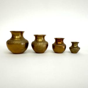 May include: Four brass vases of varying sizes, all with an ornate design. The vases are arranged in a row from largest to smallest.