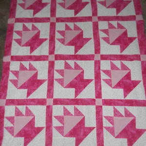 May include: A pink and white quilt with a repeating pattern of pink paw prints. The quilt is made of a soft, textured fabric.