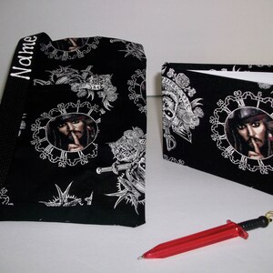 May include: Black and white fabric tote bag with a repeated pattern of a clock face with a portrait of Captain Jack Sparrow. The bag has a black strap and the word "Name" is embroidered on the strap. A matching black and white fabric notebook with a similar pattern is also shown.