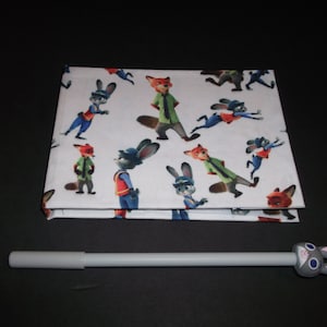 Peut inclure: Un tissu blanc pli&eacute; avec un motif r&eacute;p&eacute;t&eacute; de personnages de dessins anim&eacute;s de renards et de lapins. Un stylo gris avec un dessus en forme de lapin est devant. Les personnages sont dans diverses poses et tenues.