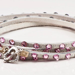 May include: A white leather wrap bracelet with pink rhinestones and a silver heart-shaped clasp.