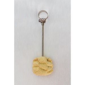 May include: A yellow fire starter with a metal handle and a clamp. The fire starter is made of woven material and is attached to a metal rod with a clamp.