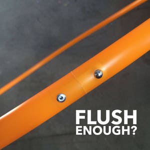 May include: Close-up of an orange plastic hoop with two silver metal rivets. The text "FLUSH ENOUGH?" is printed below the hoop.