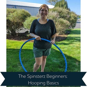 May include: A woman is holding a blue hula hoop in front of her. She is wearing a gray shirt and dark blue shorts. The background is a grassy area with trees and a building in the distance. The text "The Spinsterz Beginners: Hooping Basics" is displayed at the bottom of the image.