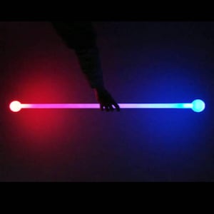 May include: A glowing, straight rod with a sphere at each end. One end glows red, the other blue, with a gradient of pink in the middle. The rod is held by a hand against a dark background.