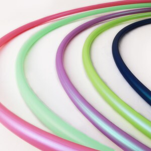 May include: Five colorful plastic hoops, arranged in a semi-circle, with a pink hoop in the foreground, followed by a light green hoop, a purple hoop, a light green hoop, and a dark blue hoop.