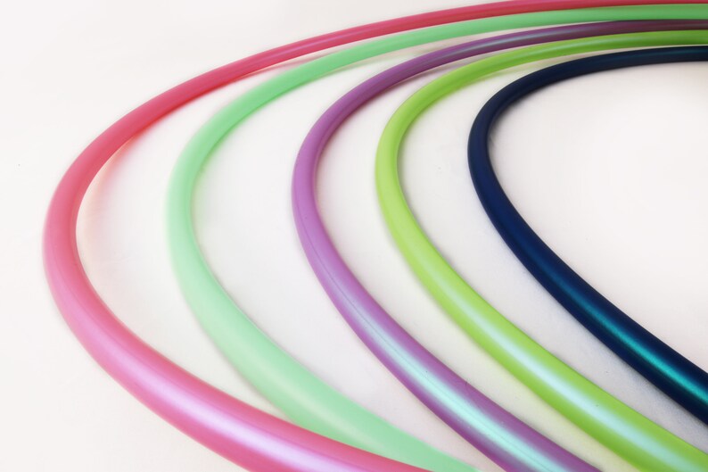 May include: Five colorful plastic hoops, arranged in a semi-circle, with a pink hoop in the foreground, followed by a light green hoop, a purple hoop, a light green hoop, and a dark blue hoop.