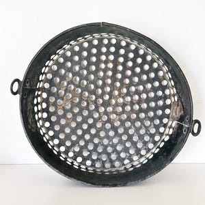 May include: A circular, black metal tray with a perforated centre. The tray has a raised rim and two small handles. The centre is filled with evenly spaced holes. The tray appears to be vintage or antique.