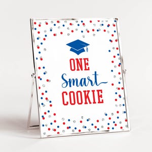 Peut inclure: Un cadre en métal argenté contenant une affiche blanche avec une icône de toque de diplômé bleue et le texte rouge et bleu ONE Smart COOKIE. La bordure présente un motif de petits points de confettis rouges, bleus et argentés.