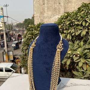 May include: A multi-strand pearl necklace with gold accents and decorative elements. The necklace is displayed on a blue mannequin.