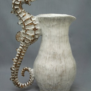 May include: White ceramic pitcher with a textured surface and a sculpted seahorse handle. The handle is brown and white.