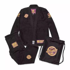Puede incluir: Gi de jiu-jitsu negro con detalles dorados y morados. El gi incluye una chaqueta, pantalones y una bolsa de cordón. La bolsa tiene el texto "Shayroll" en letras doradas.
