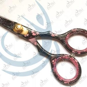 May include: A pair of black and pink hair cutting shears with a gold accent. The shears have a pink and black marbled design.